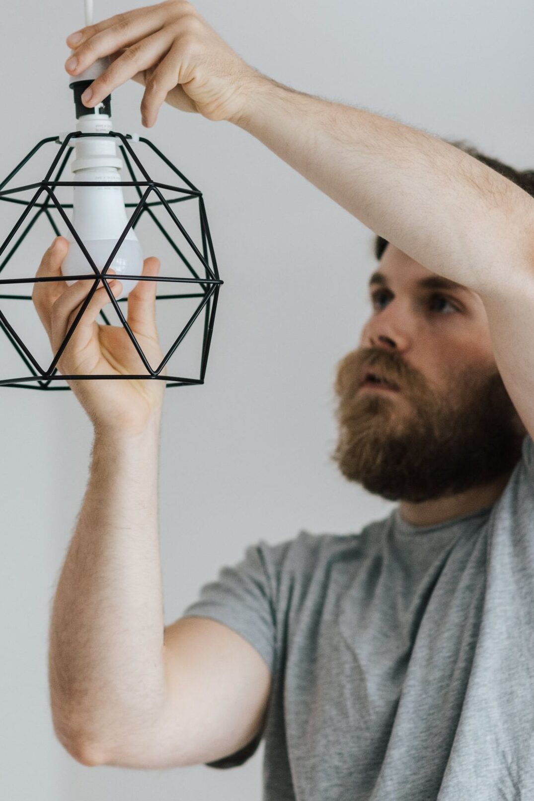 Concentrated repairman screwing light bulb in stylish lamp hanging on ceiling of new flat